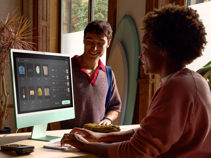 شخصان في غرفة مضاءة جيداً، أحدهما يتحقق من طلب على iMac أخضر بشريحة M4‏.