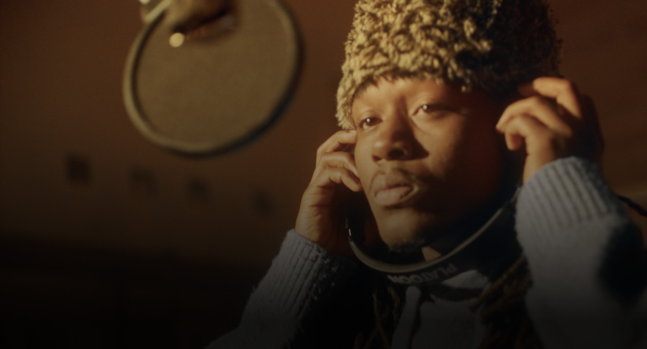 Foto von Kiddo K im Studio stehend vor einem Aufnahmemikrofon und mit Kopfhörern